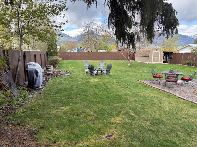 view of yard with a shed, a fenced backyard, a mountain view, an outdoor structure, and a fire pit