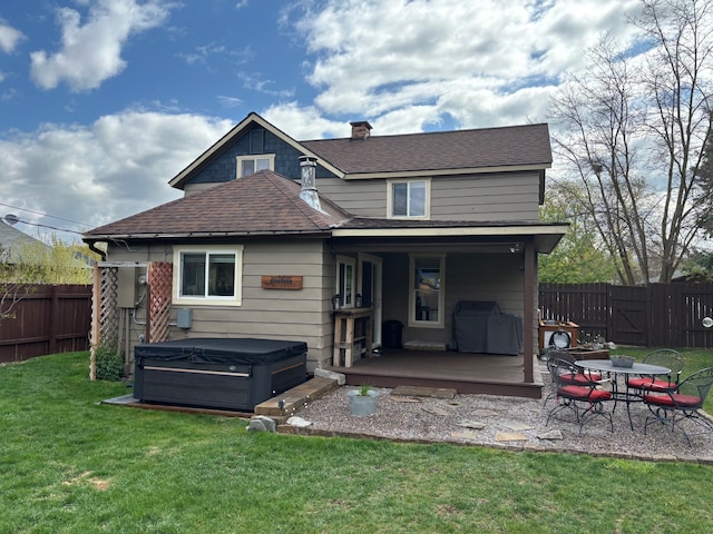 back of house with roof with shingles, a wooden deck, a hot tub, a fenced backyard, and a yard