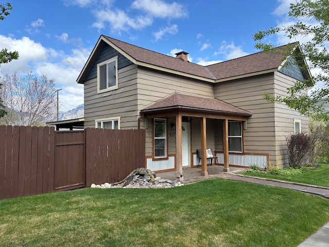 traditional-style home with a porch, a front lawn, roof with shingles, and fence