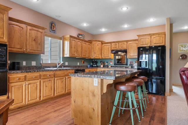 kitchen featuring a kitchen bar, a center island, under cabinet range hood, a sink, and black appliances