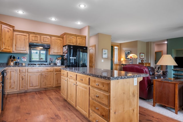 kitchen featuring open floor plan, a center island, under cabinet range hood, light wood-style flooring, and black fridge