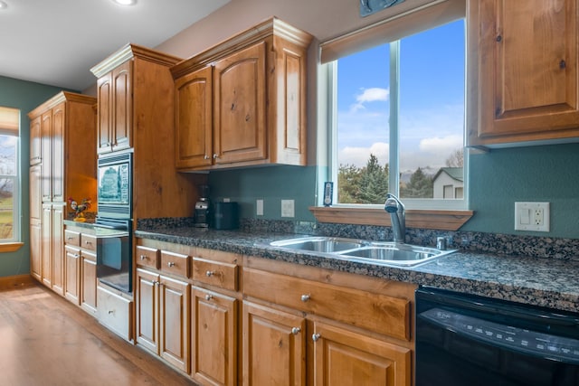 kitchen featuring dark countertops, brown cabinets, light wood-type flooring, a sink, and black appliances