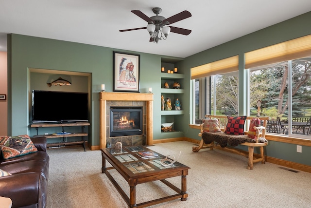 living room with a ceiling fan, a fireplace, built in shelves, carpet floors, and baseboards