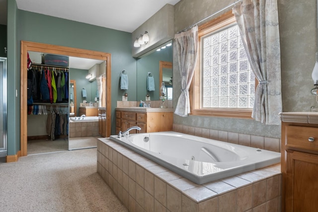 full bath with vanity, a healthy amount of sunlight, a spacious closet, and a jetted tub