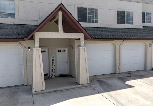 property entrance with a garage, roof with shingles, and stucco siding