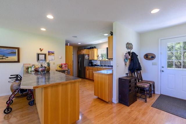kitchen featuring light wood finished floors, black refrigerator with ice dispenser, and a breakfast bar area