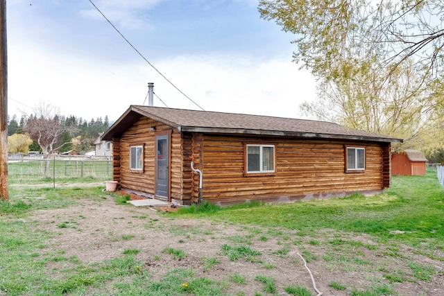 rear view of property featuring fence, log exterior, a shingled roof, and an outbuilding