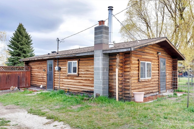 view of side of property featuring roof with shingles, fence, a chimney, and log siding
