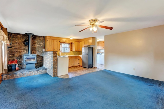 kitchen with ceiling fan, a wood stove, freestanding refrigerator, washer / dryer, and light carpet