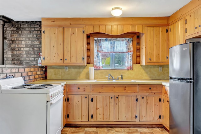 kitchen with electric range, light brown cabinetry, light countertops, a sink, and freestanding refrigerator