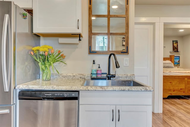 kitchen with light stone countertops, appliances with stainless steel finishes, a sink, light wood-style floors, and white cabinetry