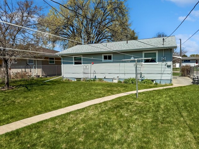 exterior space with a yard, fence, and roof with shingles