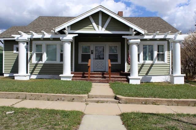 bungalow-style house featuring covered porch, a chimney, and roof with shingles