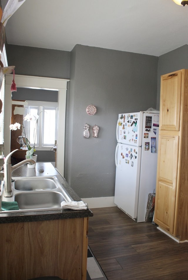 kitchen featuring dark wood-style flooring, dark countertops, a sink, freestanding refrigerator, and baseboards