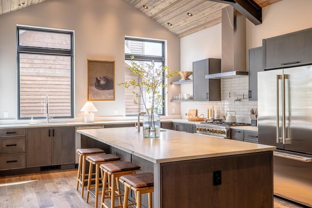 kitchen featuring appliances with stainless steel finishes, a sink, light wood finished floors, wall chimney exhaust hood, and a kitchen island
