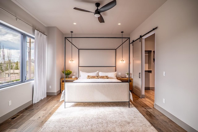 bedroom with recessed lighting, baseboards, a barn door, and wood finished floors