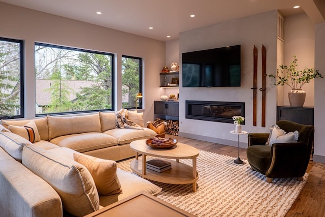 living area with recessed lighting, a glass covered fireplace, and wood finished floors