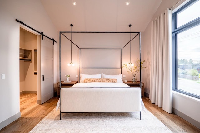bedroom featuring baseboards, a walk in closet, light wood-type flooring, a barn door, and recessed lighting