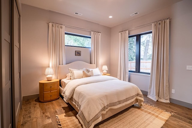 bedroom featuring baseboards, visible vents, multiple windows, and wood finished floors