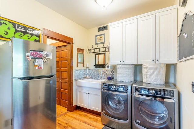 washroom featuring visible vents, cabinet space, washer and dryer, and light wood-type flooring