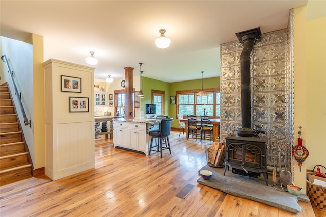 kitchen with white cabinets, a breakfast bar, a wood stove, light wood-style floors, and baseboards