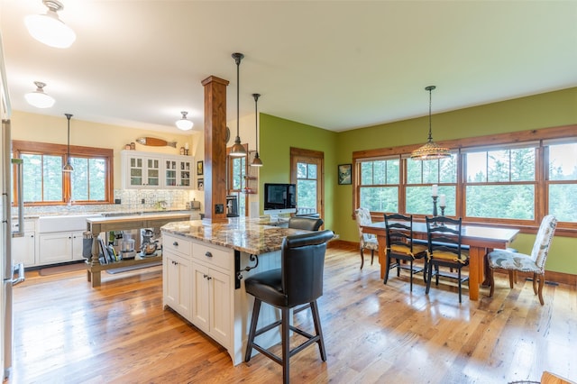 kitchen featuring light stone counters, white cabinetry, decorative backsplash, light wood-type flooring, and glass insert cabinets