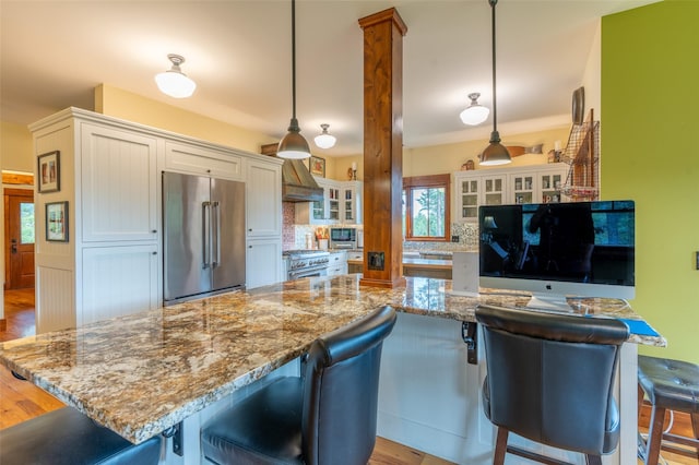 kitchen with light stone countertops, a kitchen breakfast bar, premium range hood, high end appliances, and tasteful backsplash