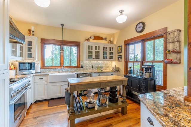 kitchen with decorative backsplash, high end stainless steel range, white cabinets, a sink, and hanging light fixtures