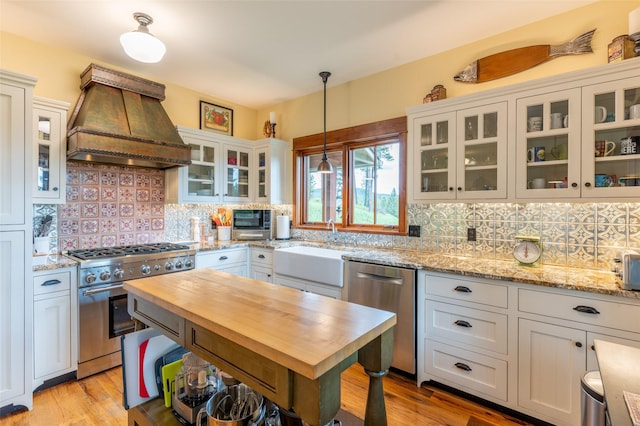 kitchen featuring decorative backsplash, premium range hood, a sink, wood counters, and appliances with stainless steel finishes