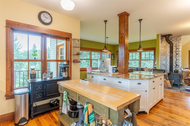 kitchen with a wood stove, a kitchen island, wooden counters, white cabinetry, and light wood-style flooring