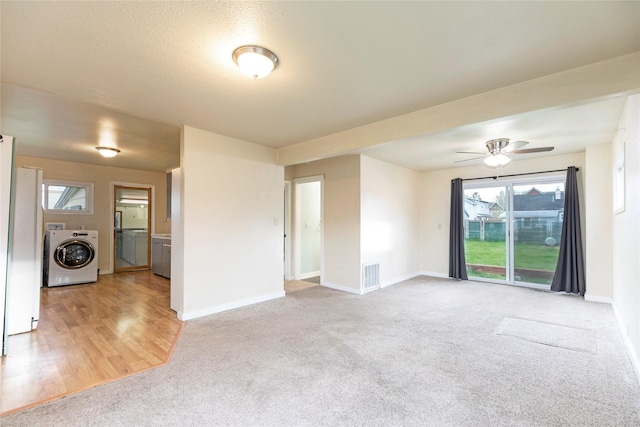 unfurnished living room featuring light colored carpet, washer / dryer, baseboards, and visible vents