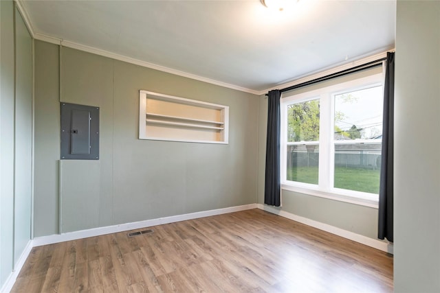 empty room featuring crown molding, visible vents, baseboards, electric panel, and light wood-style flooring