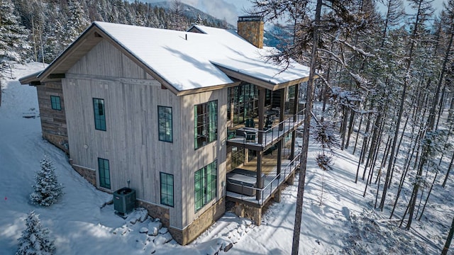 view of snowy exterior featuring cooling unit, a chimney, and a mountain view