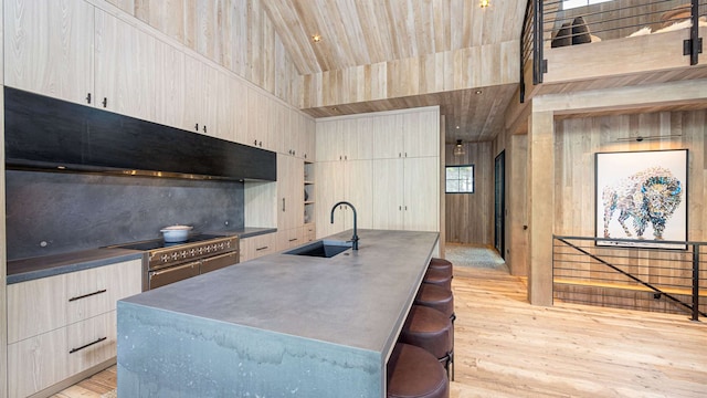 kitchen with wood walls, light wood-type flooring, range with two ovens, a sink, and vaulted ceiling