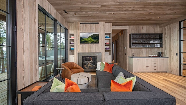 living area featuring wood finished floors, a fireplace, indoor wet bar, wooden walls, and wooden ceiling