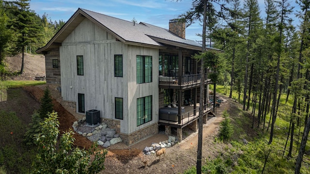 rear view of property with a deck, cooling unit, a chimney, and stone siding