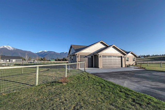 view of side of property featuring fence, an attached garage, a mountain view, a lawn, and driveway