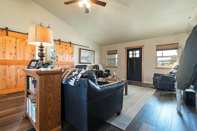 living area featuring a barn door, dark wood-style flooring, ceiling fan, and vaulted ceiling