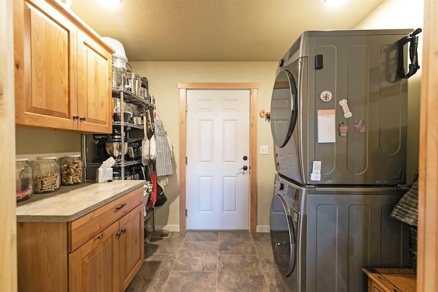 washroom with baseboards, stone finish floor, stacked washer and dryer, and cabinet space