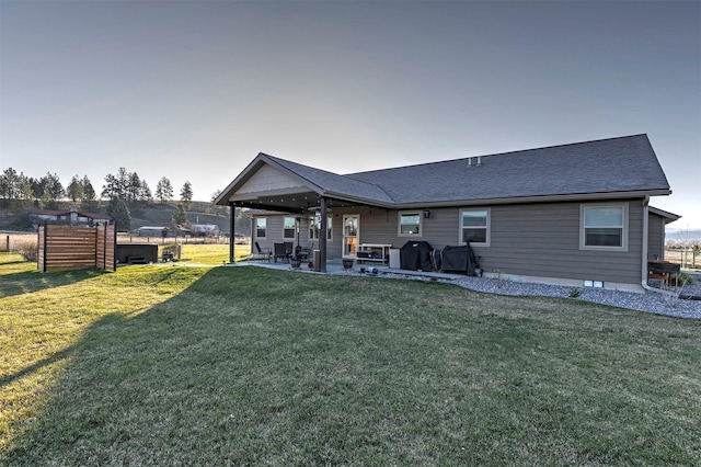 back of property with a lawn, a patio, fence, and a shingled roof