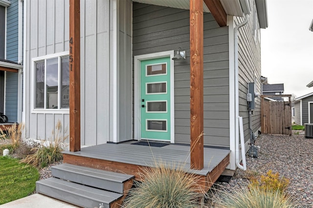 entrance to property with board and batten siding, fence, and central air condition unit