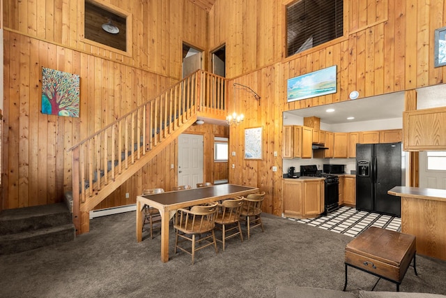 carpeted dining space featuring a baseboard radiator, a high ceiling, wood walls, and stairs