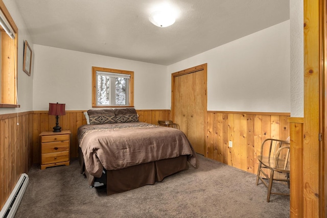 carpeted bedroom with a closet, a baseboard heating unit, wooden walls, and a wainscoted wall