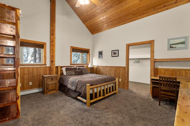 carpeted bedroom with wooden walls, multiple windows, baseboard heating, high vaulted ceiling, and a wainscoted wall