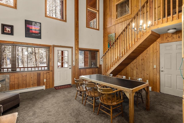 carpeted dining area with wooden walls, a high ceiling, baseboard heating, and stairs