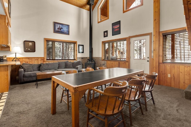 carpeted dining room with wainscoting, a high ceiling, a wood stove, and wood walls