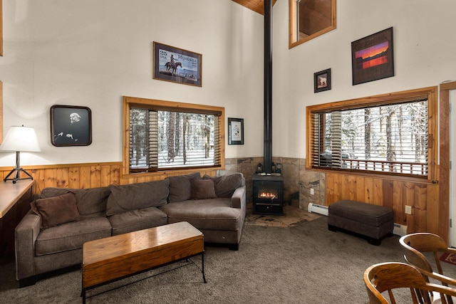 carpeted living room with wood walls, a wealth of natural light, a wood stove, and a wainscoted wall
