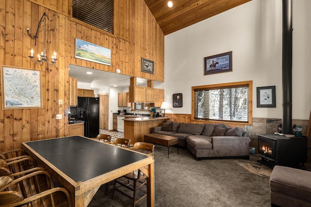 living room with wooden walls, a wood stove, high vaulted ceiling, carpet, and a wainscoted wall