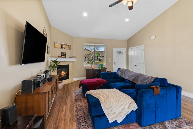 living area with ceiling fan, a tiled fireplace, recessed lighting, baseboards, and wood finished floors