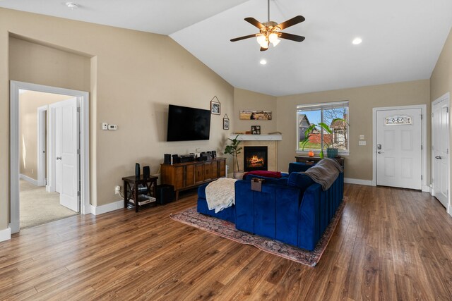living room with a warm lit fireplace, ceiling fan, baseboards, wood finished floors, and lofted ceiling